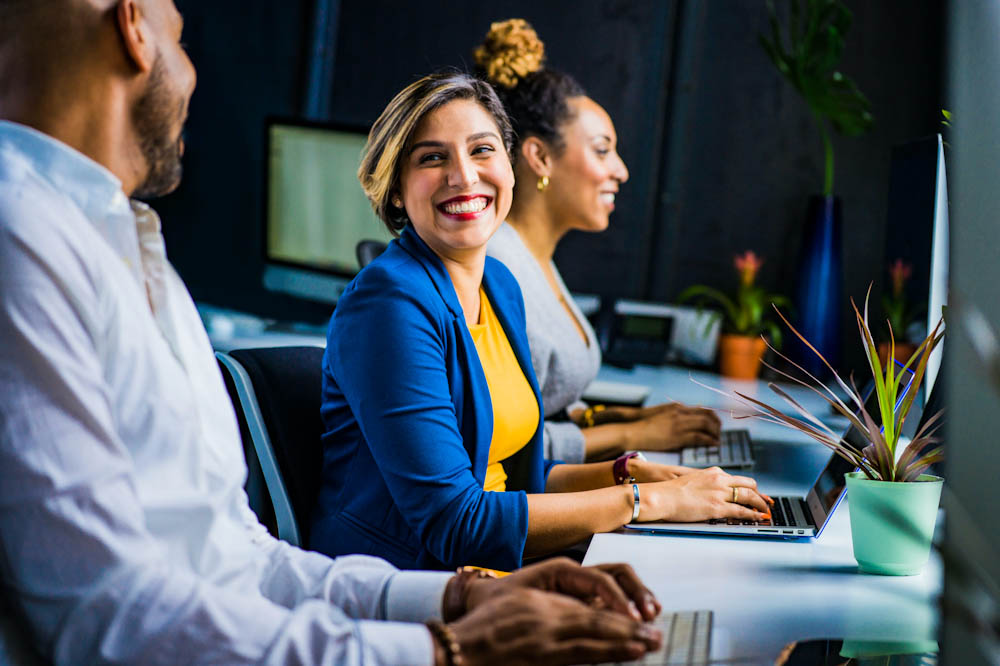 Woman at laptop smiling with coworkers